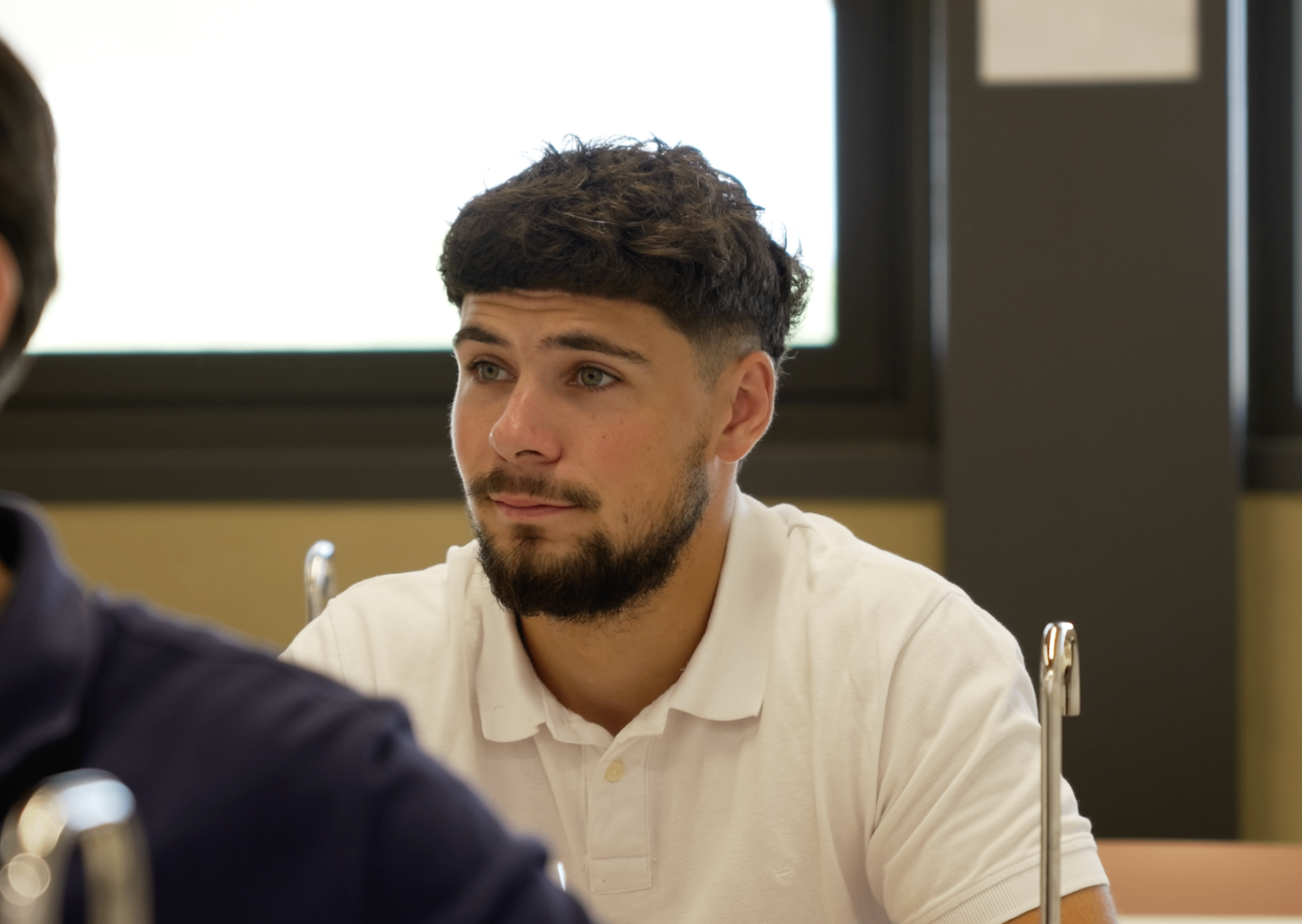 Jeune membre barbu en polo blanc attentif pendant la masterclass