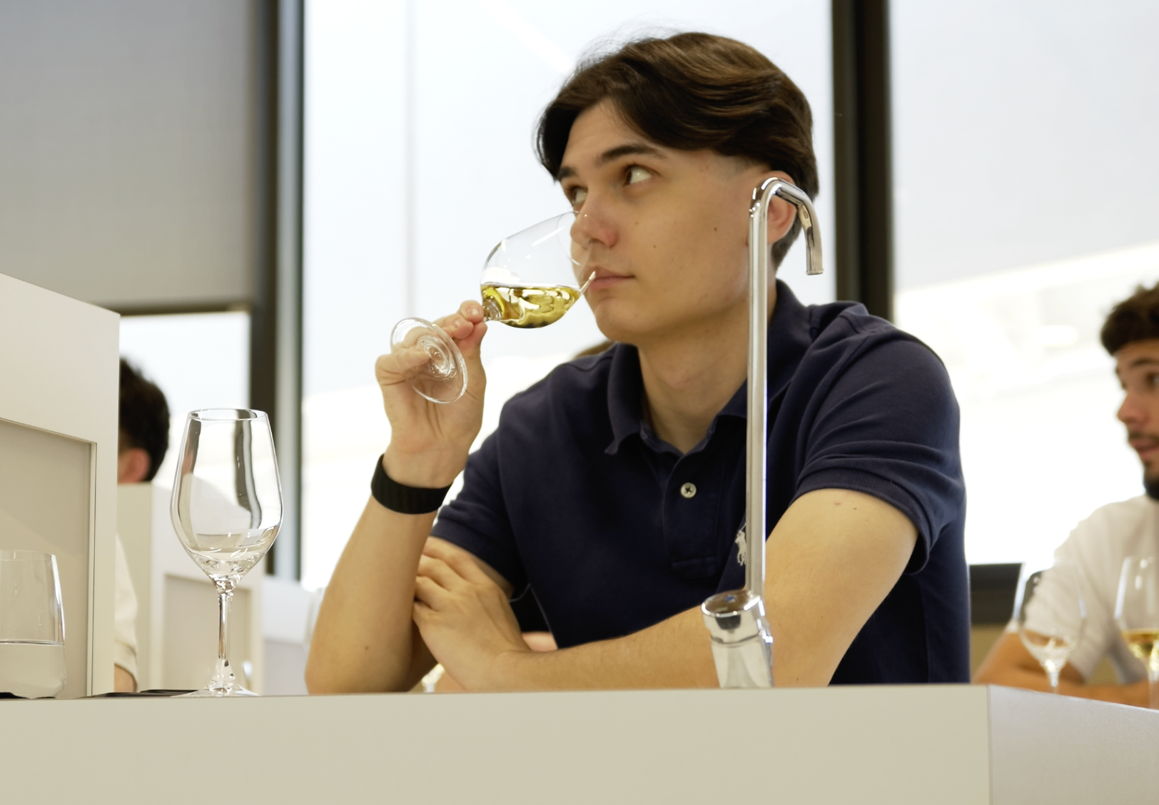 Jeune membre en polo marine dégustant un vin blanc de profil