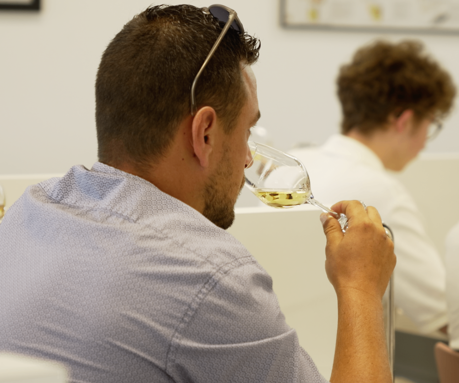 Membre en chemise bleue dégustant au nez un verre de vin blanc