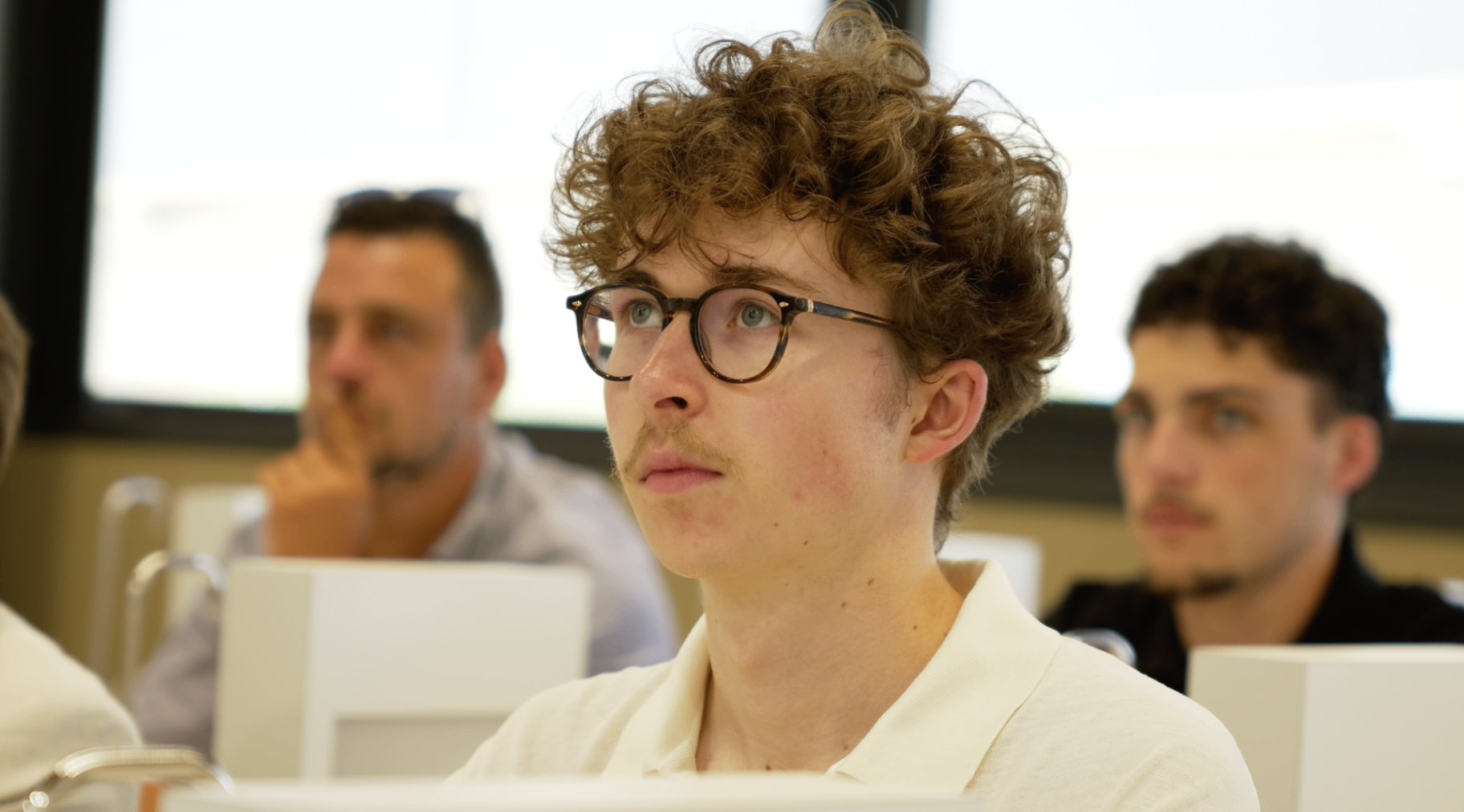 Jeune membre bouclé en polo blanc écoutant attentivement la présentation