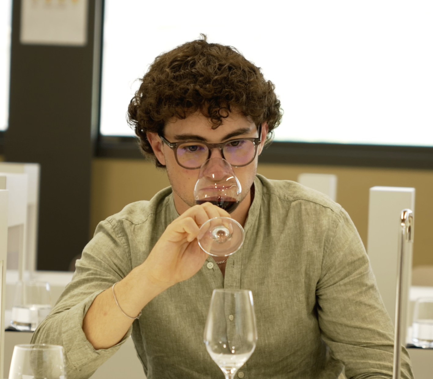 Jeune membre aux cheveux bouclés dégustant un verre face caméra