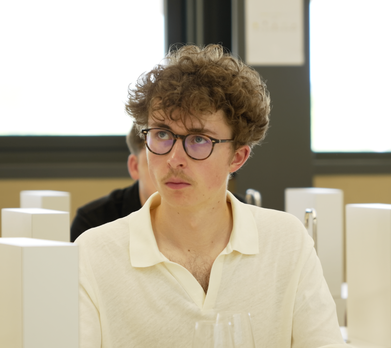 Jeune membre bouclé en polo blanc face caméra pendant la masterclass